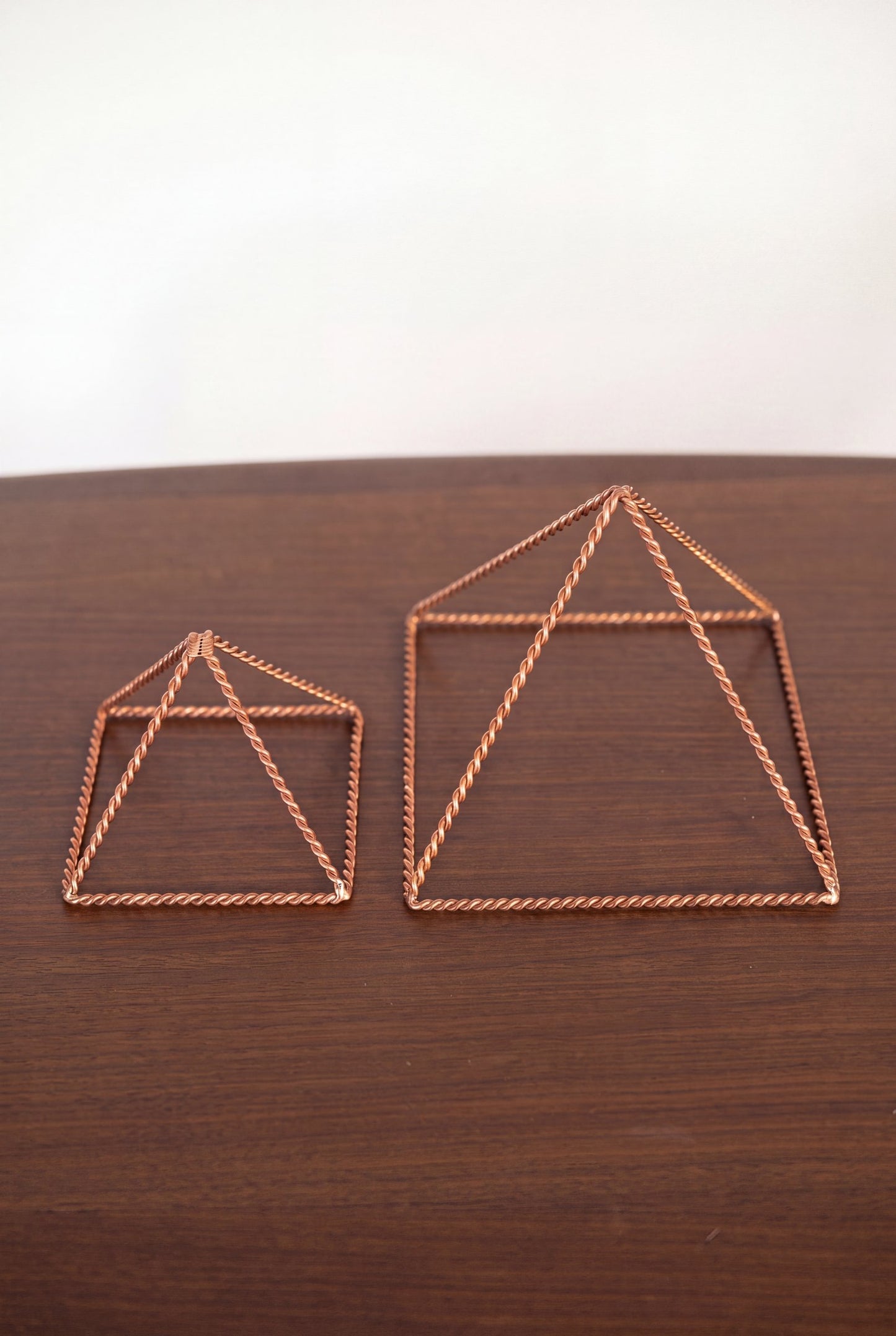 Pyramide énergisante en cuivre torsadé Kopero, les deux tailles côte à côte sur une table en bois
