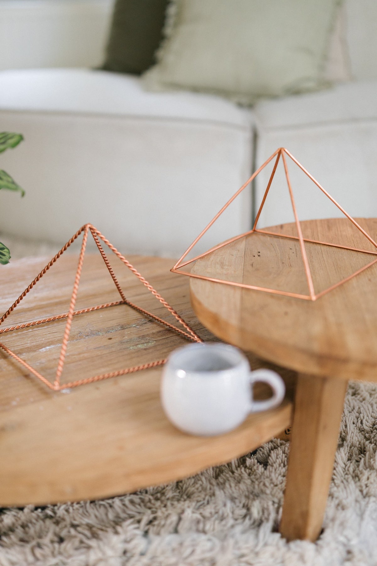 Kopero Pyramide énergisante en cuivre lisse Grande (23,56 cm), une grande pyramide torsadée et une grande pyramide lisse sur deux tables en bois avec un mug