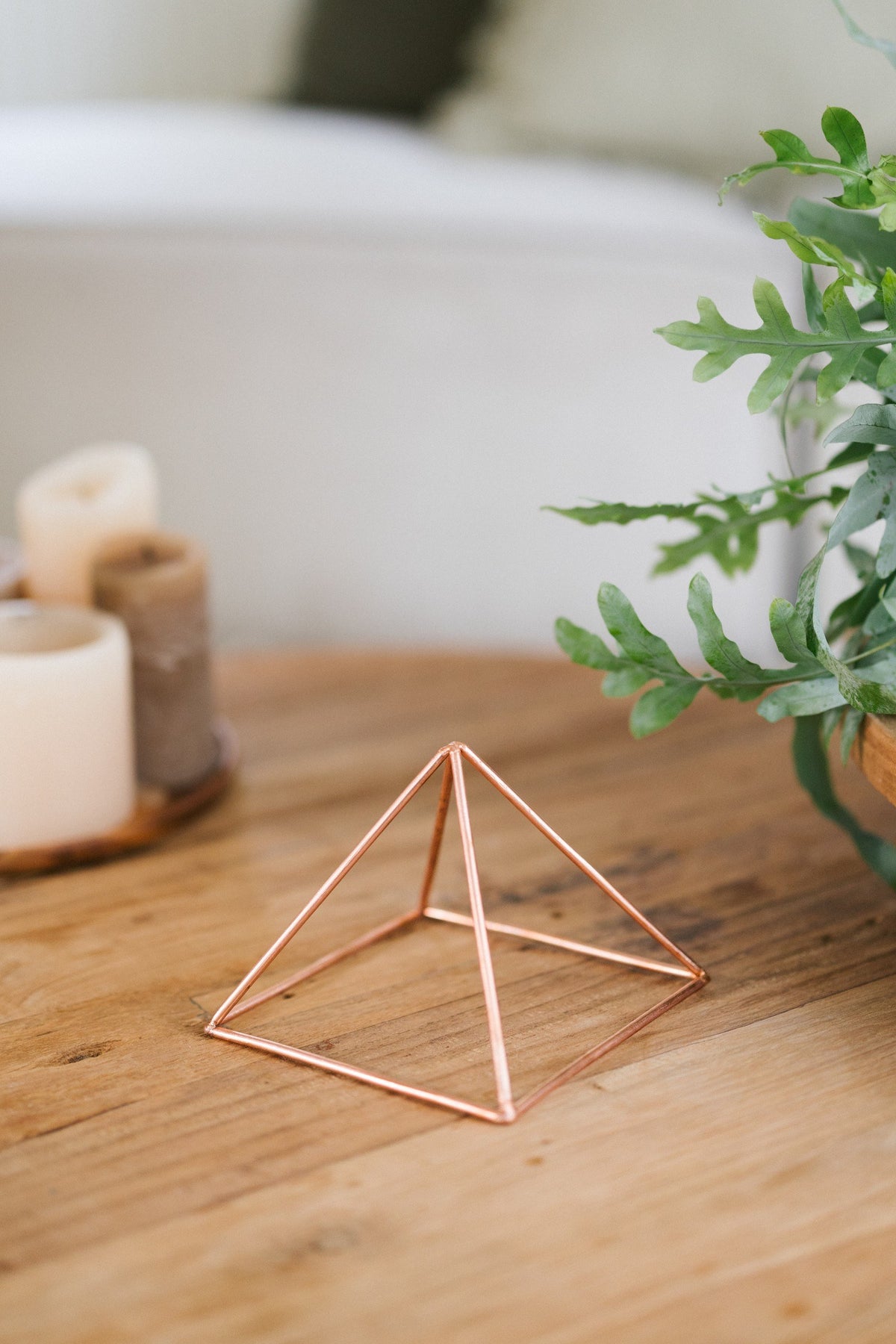 Kopero Pyramide énergisante en cuivre lisse Petite (14,56 cm), sur une table en bois à côté de bougies