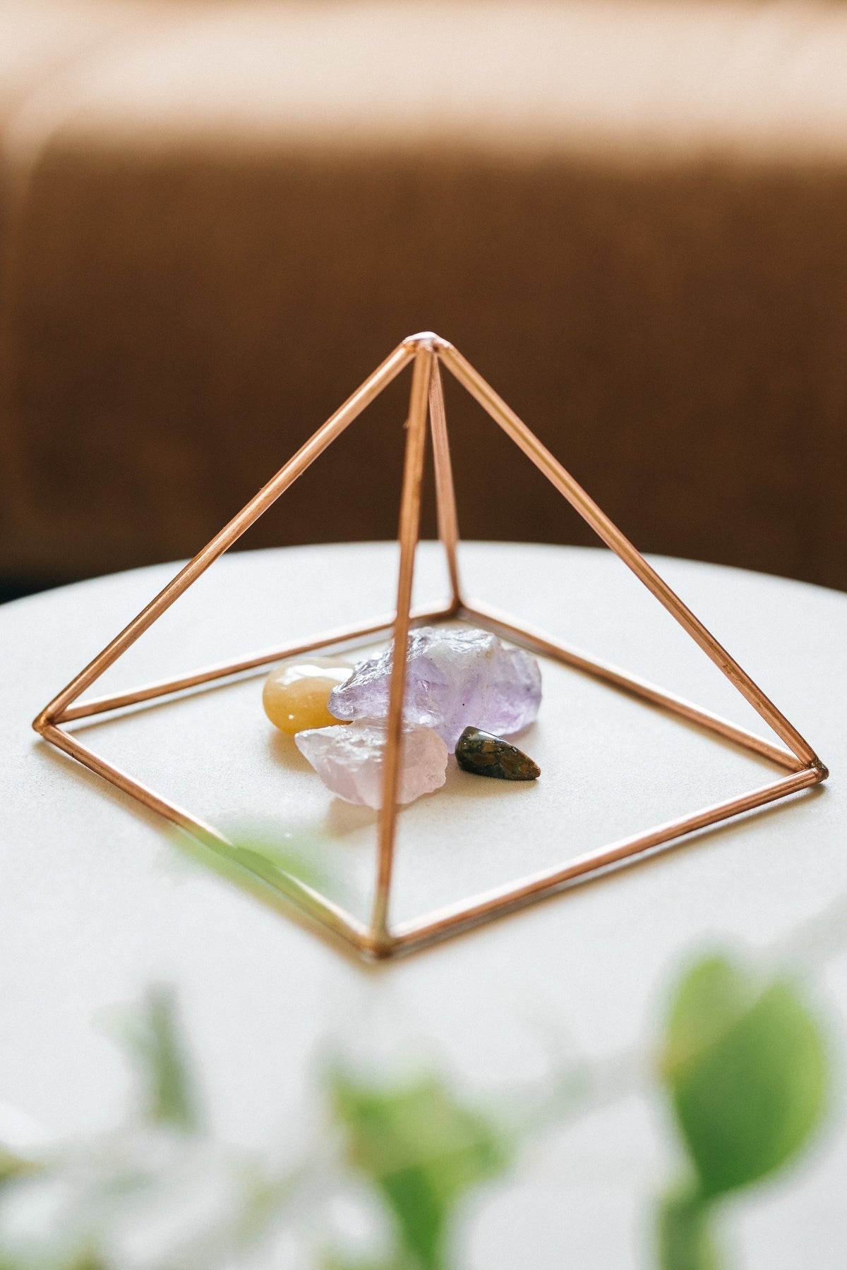 Kopero Pyramide énergisante en cuivre lisse Petite (14,56 cm), avec des pierres précieuses dessous sur une petite table blanche