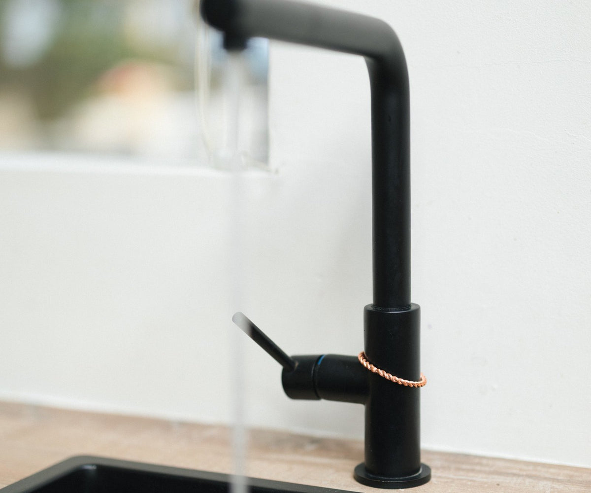 Kopero Koperen Tensorring, om de kraan van een zwarte keukenkraan met stromend water