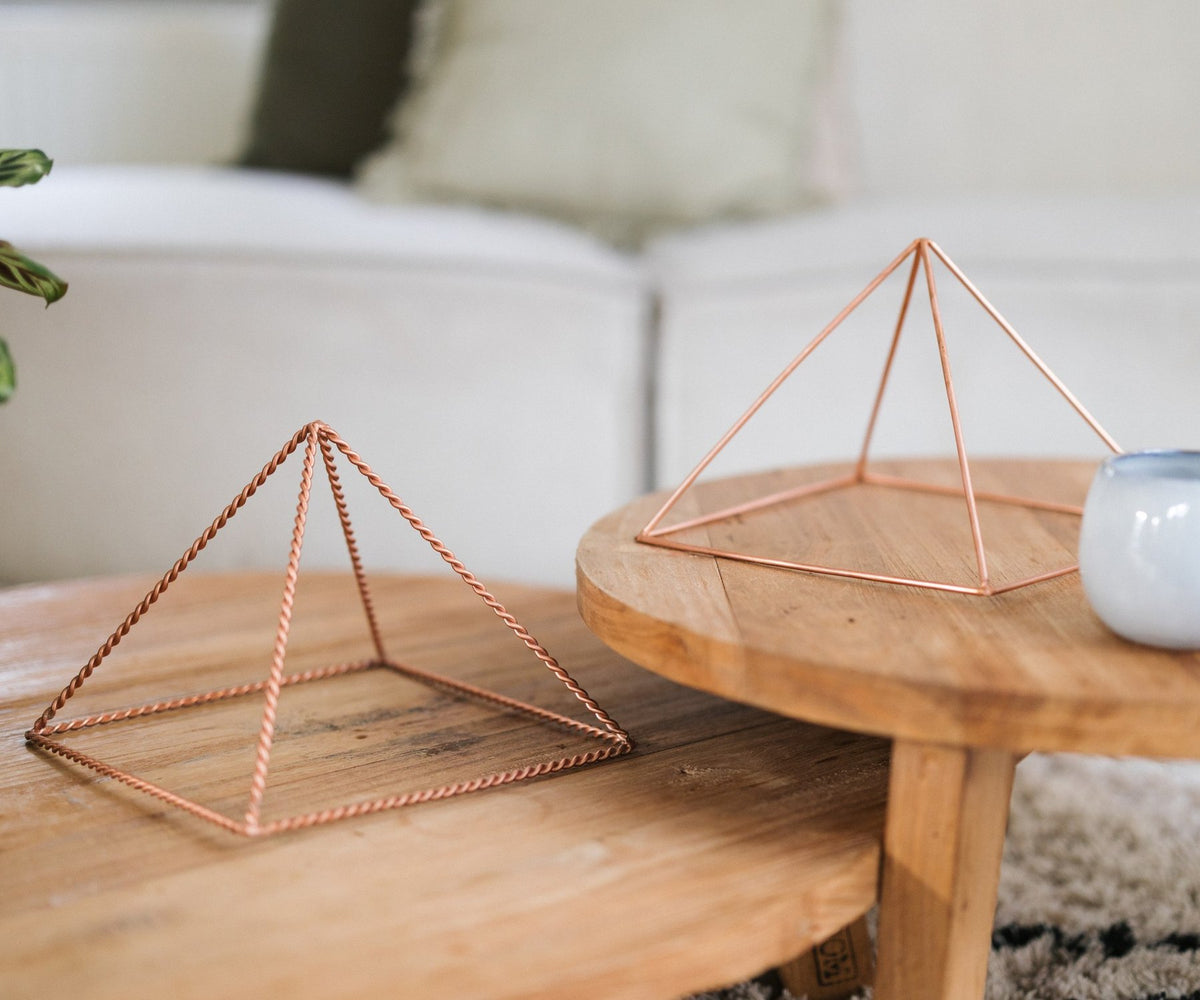 Een gedraaide en een gladde koperen piramide op een houten tafel voor een bank