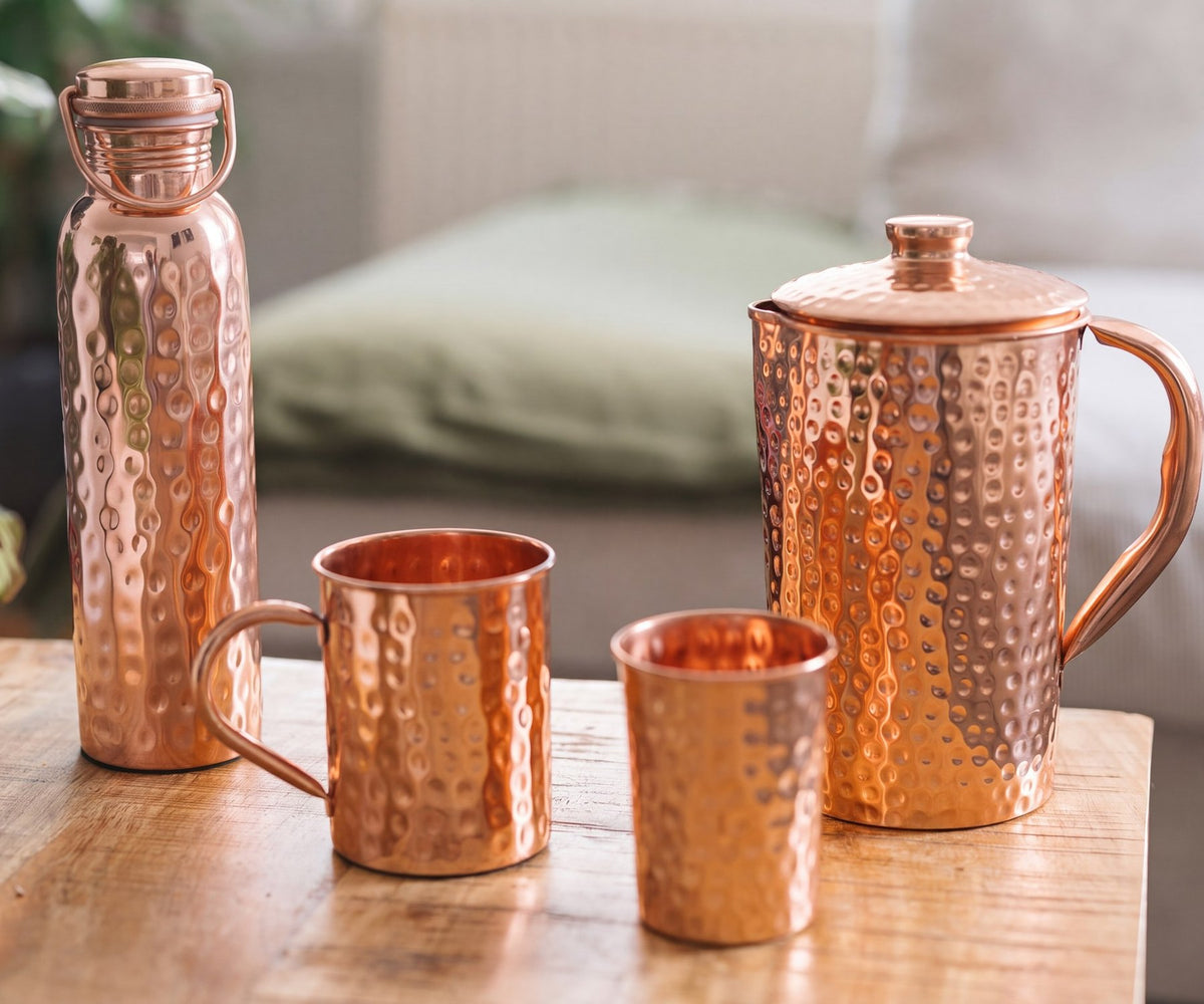 Gehamerde koperen waterfles, mok, beker en kan op een houten tafel voor een bank