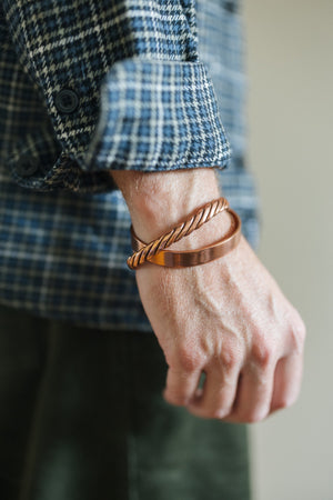 Kopero Koperen Armband Gedraaid, om de pols over een geruite overhemdsmouw, samen met een gladde armband