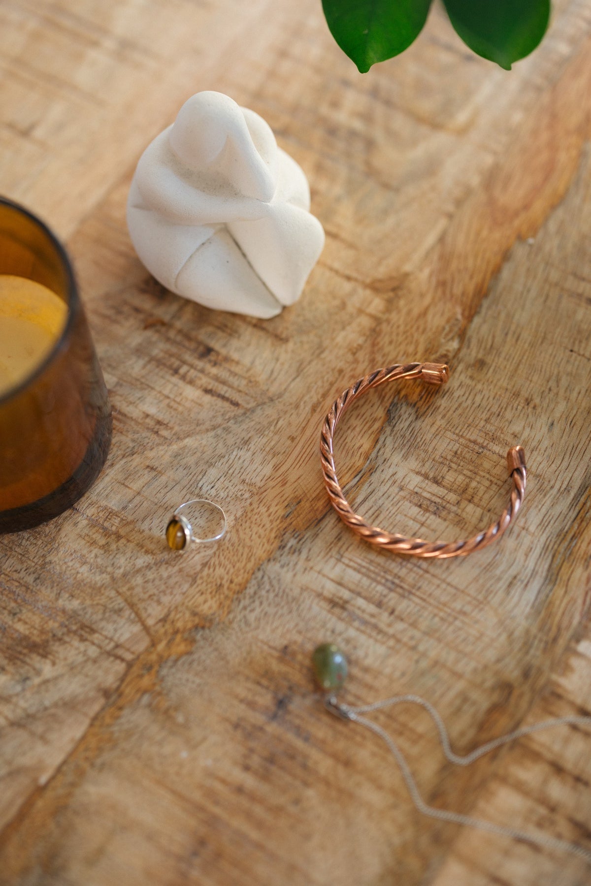 Kopero Koperen Armband Gedraaid, op een houten tafel naast een beeldje en een ring