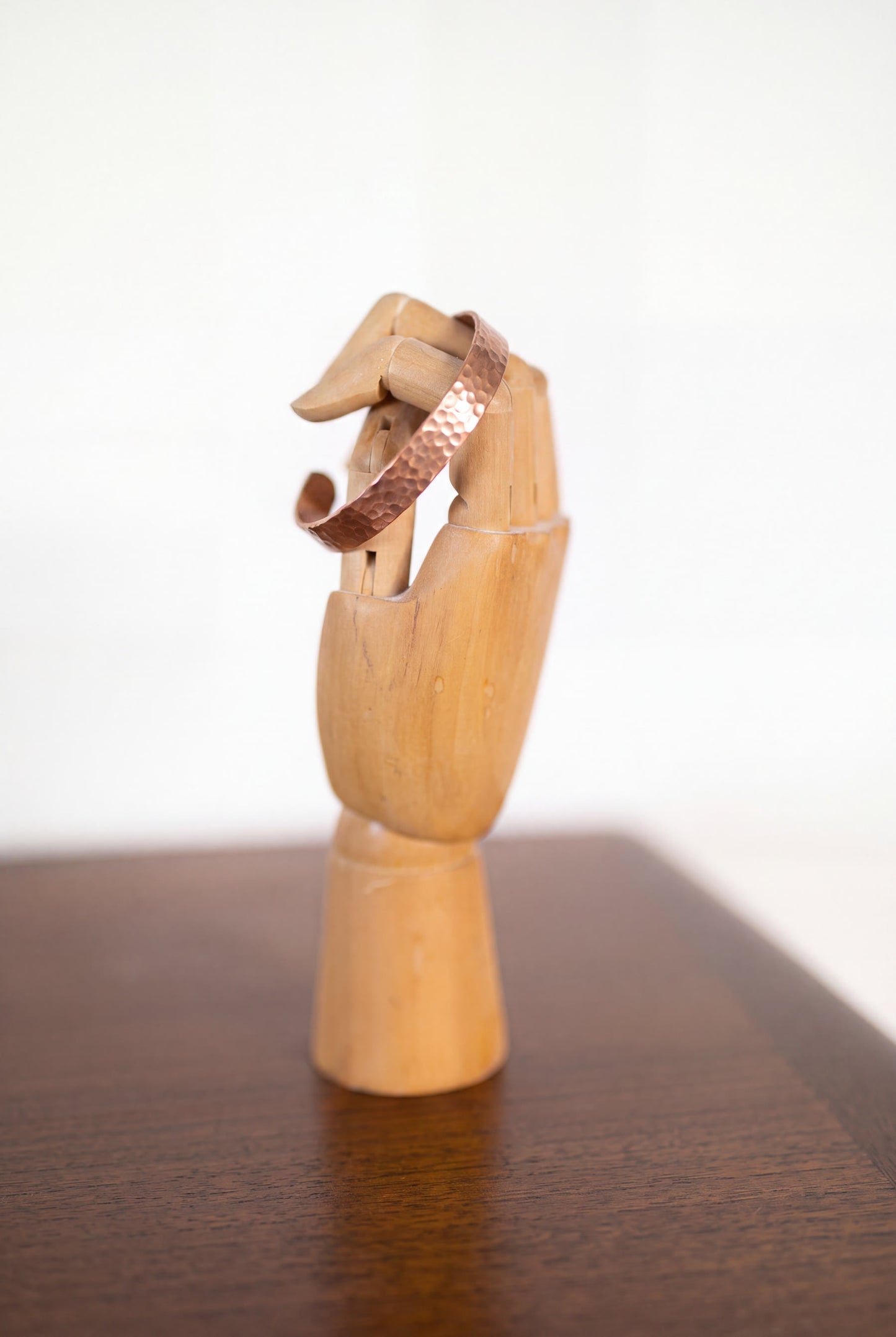 Bracelet en cuivre martelé Kopero sur une main à bijoux en bois