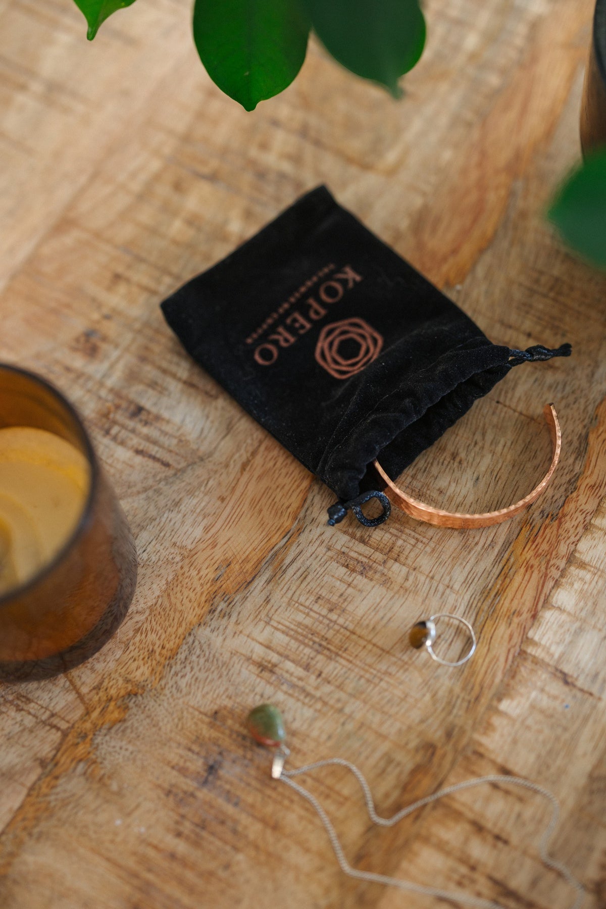 Kopero Koperen Armband Gehamerd, op een houten tafel naast de fluwelen draagzak, een kaars en sieraden