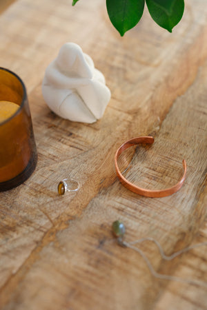 Kopero Koperen Armband Glad, op een houten tafel naast een beeldje en een ring