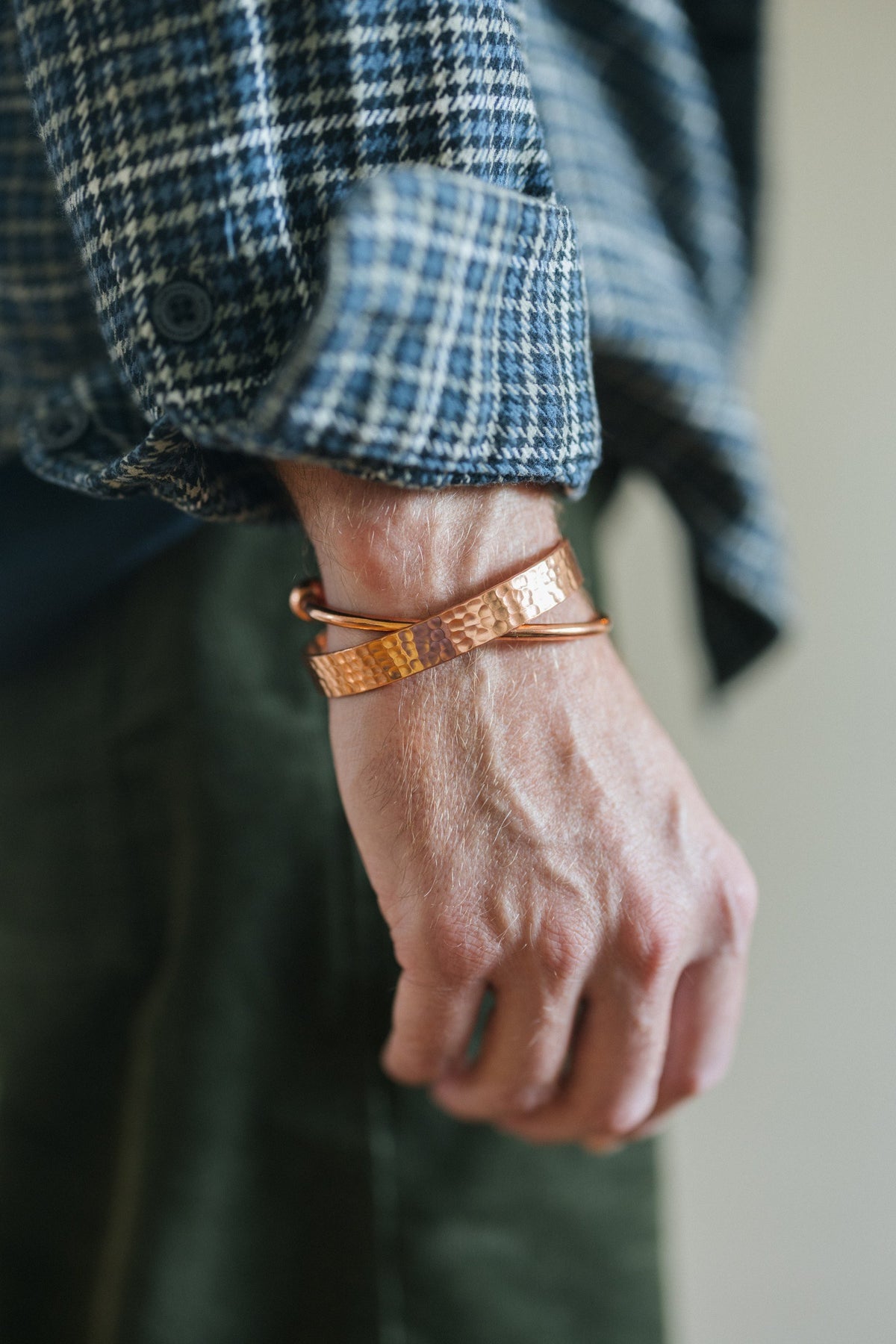 Kopero Koperen Armband Rond, om de pols over een geruite overhemdsmouw, samen met een gehamerde armband