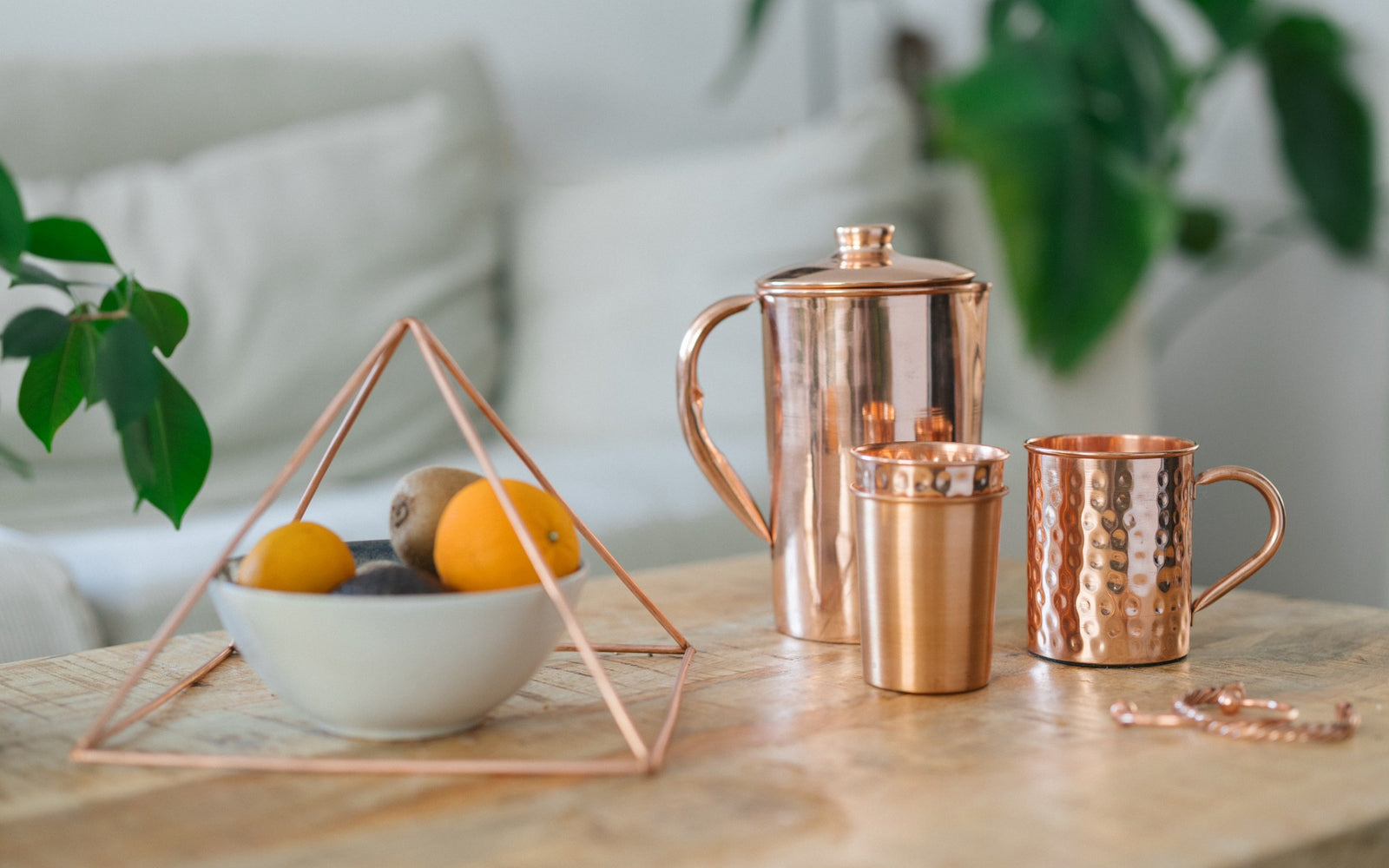 Pyramide en cuivre au-dessus d'une coupe de fruits, avec une cruche, un gobelet, un mug et un bracelet sur une table en bois
