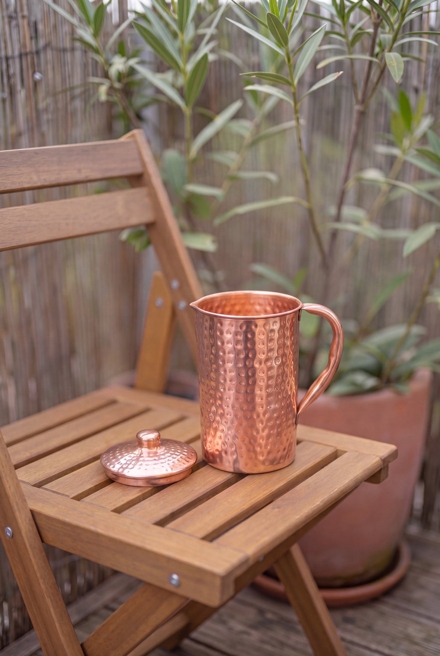 Cruche en cuivre Kopero Martelée en extérieur sur une chaise de jardin en bois, avec le couvercle à côté