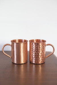 Mug en cuivre Kopero, les deux finitions côte à côte sur une table en bois