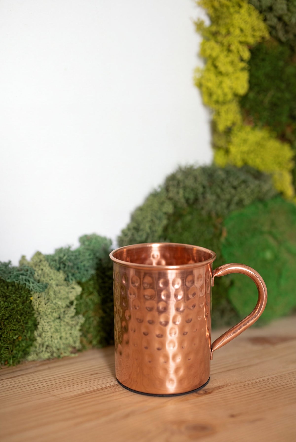 Mug en cuivre Kopero Martelé devant un tableau de mousse sur une étagère en pin