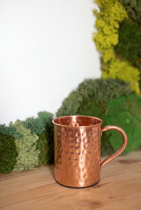 Mug en cuivre Kopero Martelé devant un tableau de mousse sur une étagère en pin
