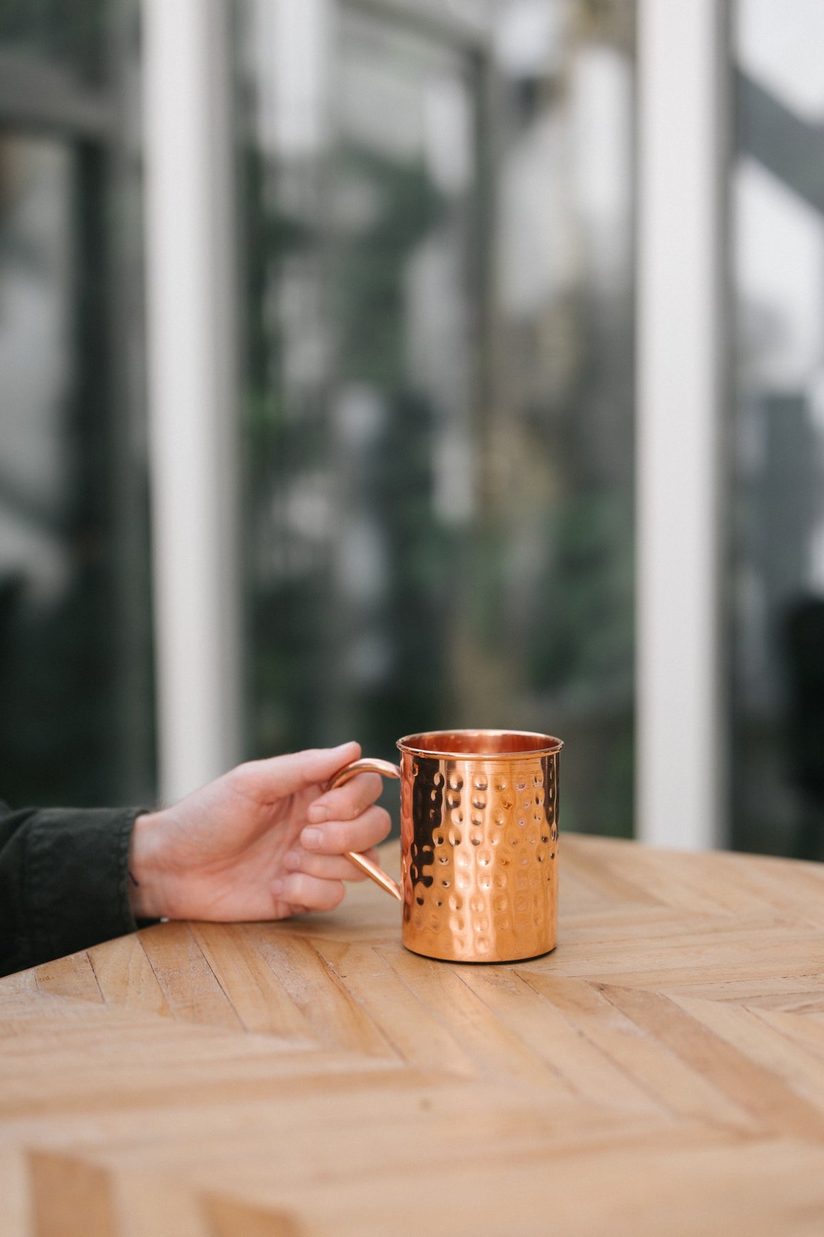 Kopero Koperen Mok Gehamerd, op een houten tafel, met een hand aan het handvat