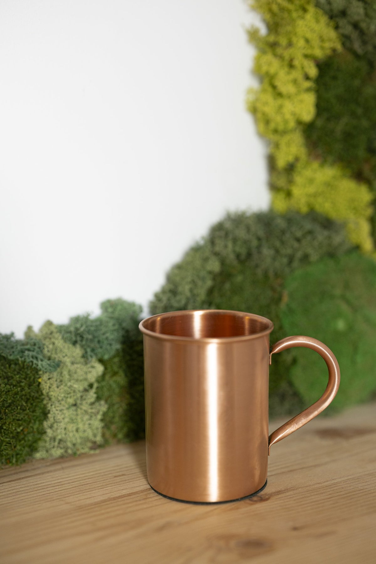 Mug en cuivre Kopero Lisse devant un tableau de mousse sur une étagère en pin