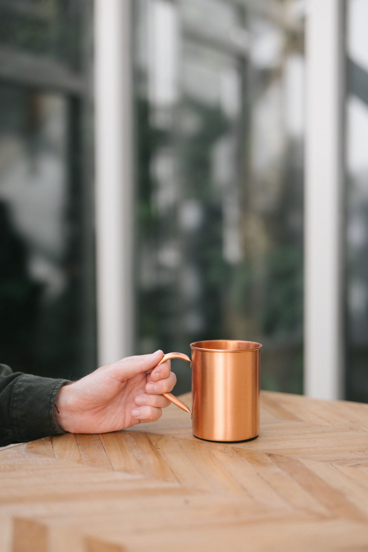 Kopero Koperen Mok Glad, op een houten tafel, met een hand aan het handvat