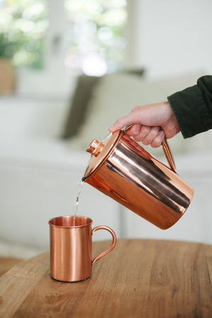 Kopero Koperen Mok Glad, terwijl er water in wordt geschonken uit een koperen kan