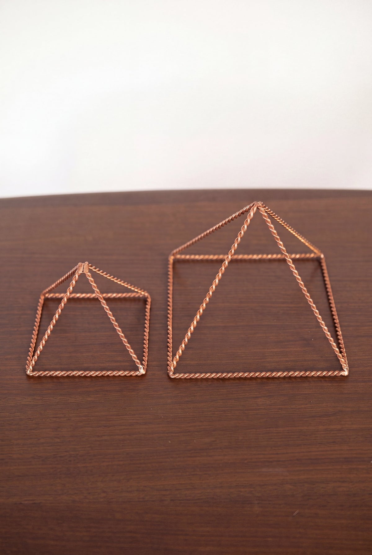 Pyramide énergisante en cuivre torsadé Kopero, les deux tailles côte à côte sur une table en bois