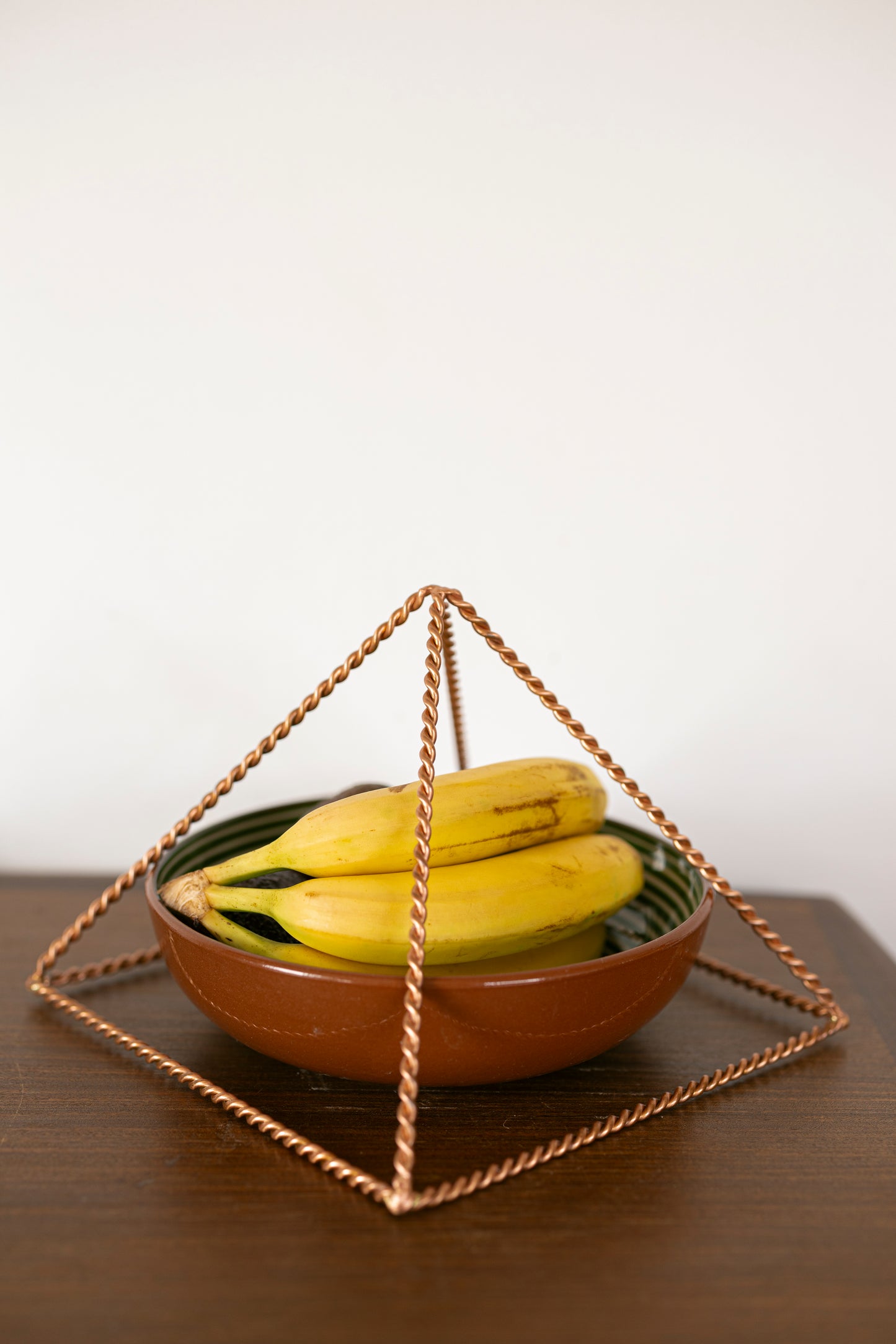 Kopero Pyramide Énergisante en Cuivre Torsadé, 23,56 cm, au-dessus d'un bol de fruits