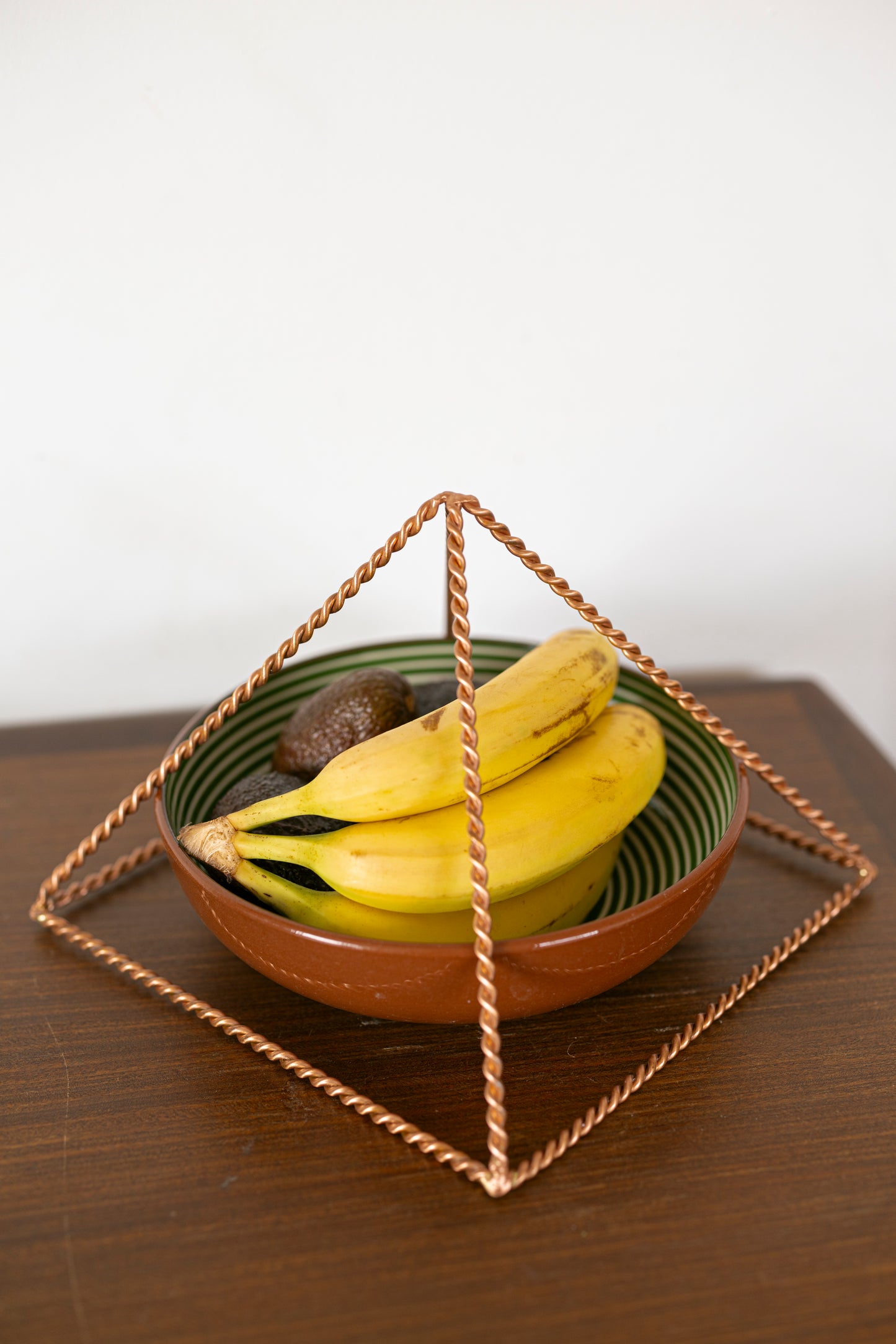 Kopero Pyramide Énergisante en Cuivre Torsadé, 23,56 cm, angle incliné au-dessus d'un bol de fruits