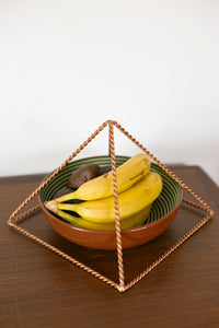 Kopero Pyramide Énergisante en Cuivre Torsadé, 23,56 cm, angle incliné au-dessus d'un bol de fruits