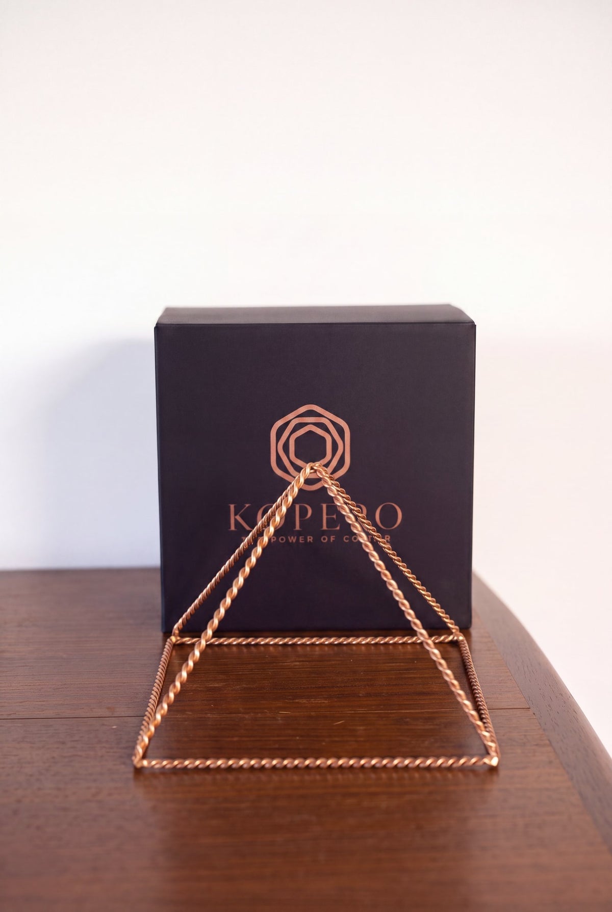 Pyramide énergisante en cuivre torsadé Kopero Grande (23,56 cm) devant le coffret cadeau noir Kopero