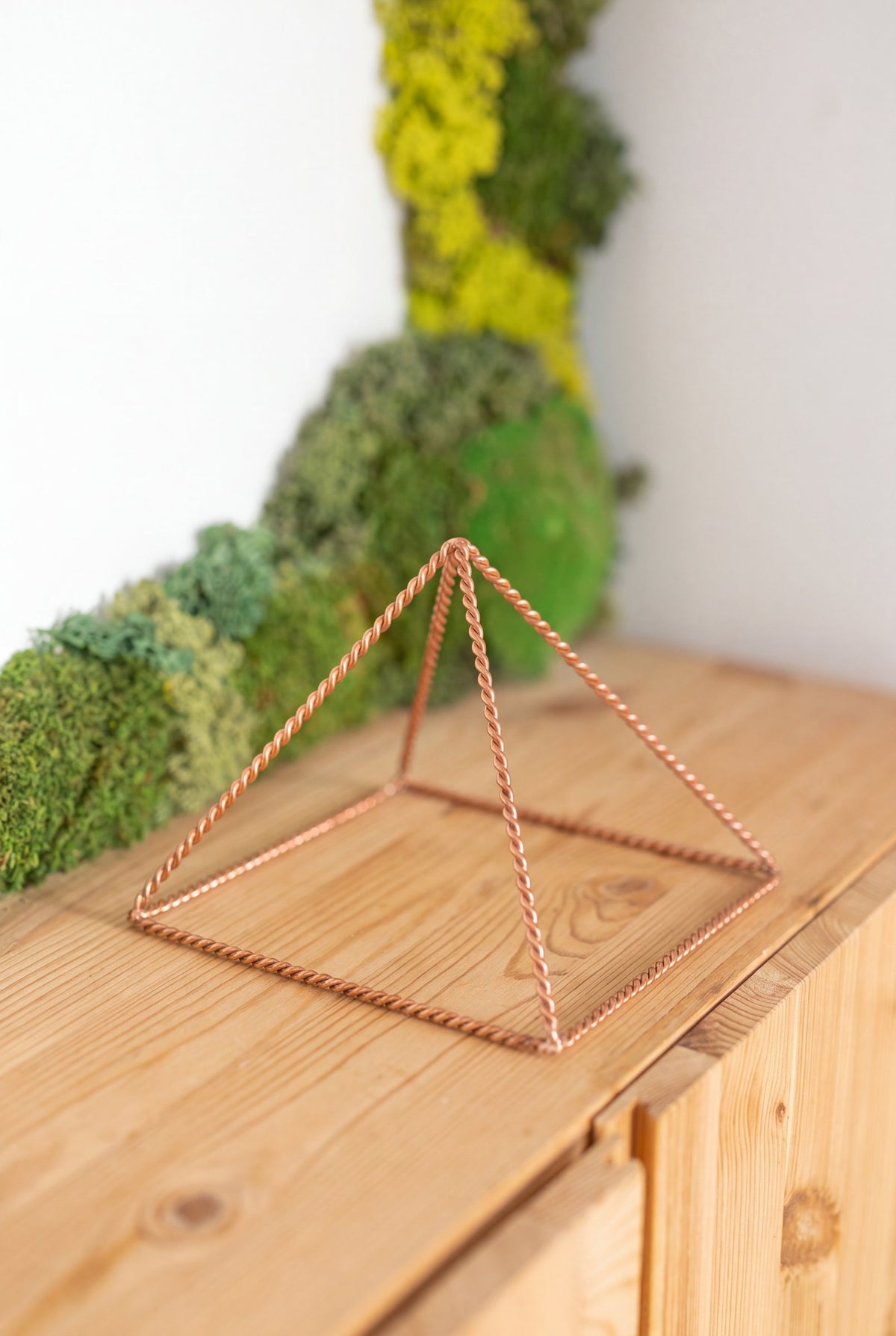 Pyramide énergisante en cuivre torsadé Kopero Petite (14,56 cm) sur une armoire en pin devant un tableau de mousse