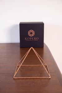 Pyramide énergisante en cuivre torsadé Kopero Petite (14,56 cm) devant le coffret cadeau noir Kopero