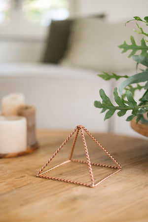 Kopero Koperen Piramide Energizer Gedraaid Klein (14,56 cm), op een houten tafel naast kaarsen