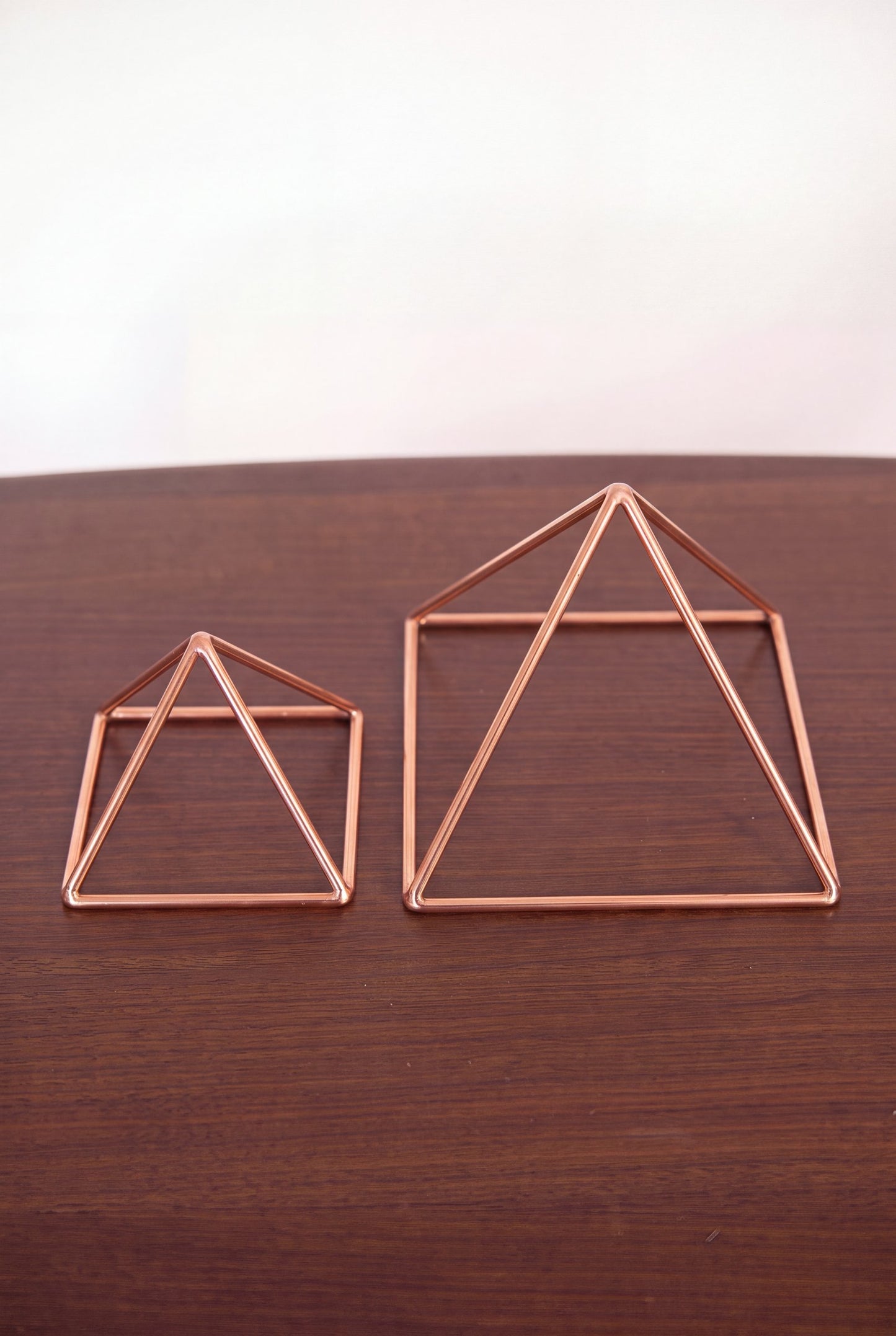 Pyramide énergisante en cuivre lisse Kopero, les deux tailles côte à côte sur une table en bois