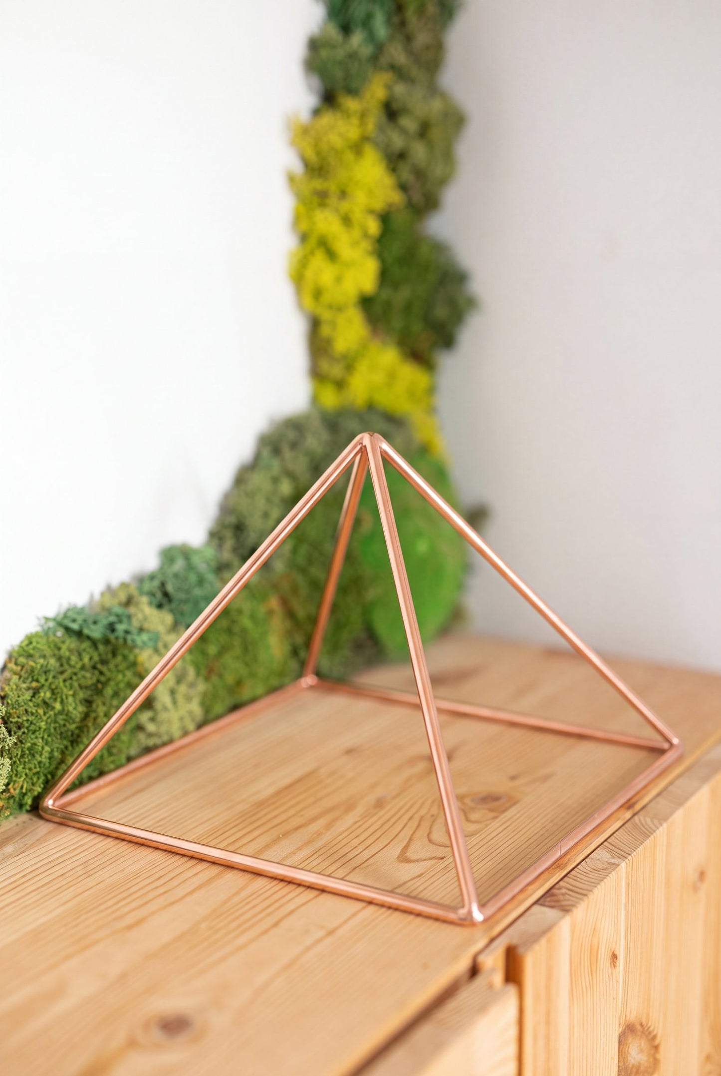 Pyramide énergisante en cuivre lisse Kopero Grande (23,56 cm) sur une armoire en pin devant un tableau de mousse