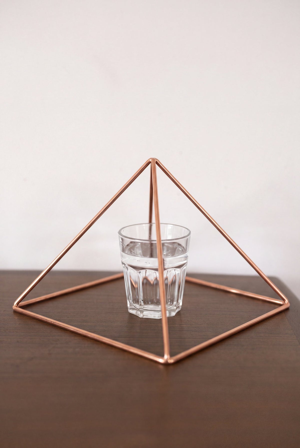 Pyramide énergisante en cuivre lisse Kopero Grande (23,56 cm) au-dessus d'un verre d'eau