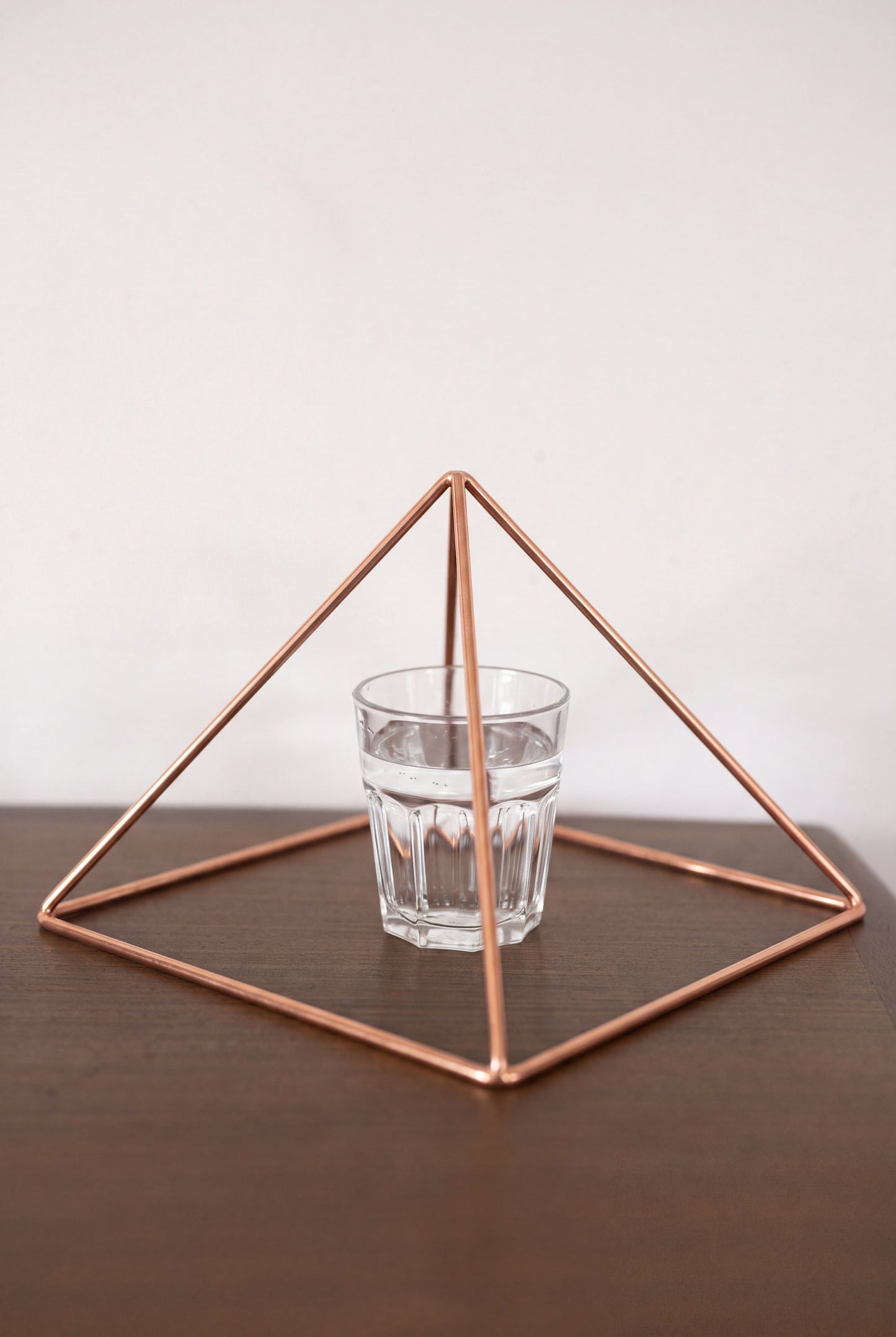 Pyramide énergisante en cuivre lisse Kopero Grande (23,56 cm) au-dessus d'un verre d'eau
