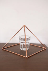 Pyramide énergisante en cuivre lisse Kopero Grande (23,56 cm) au-dessus d'un verre d'eau