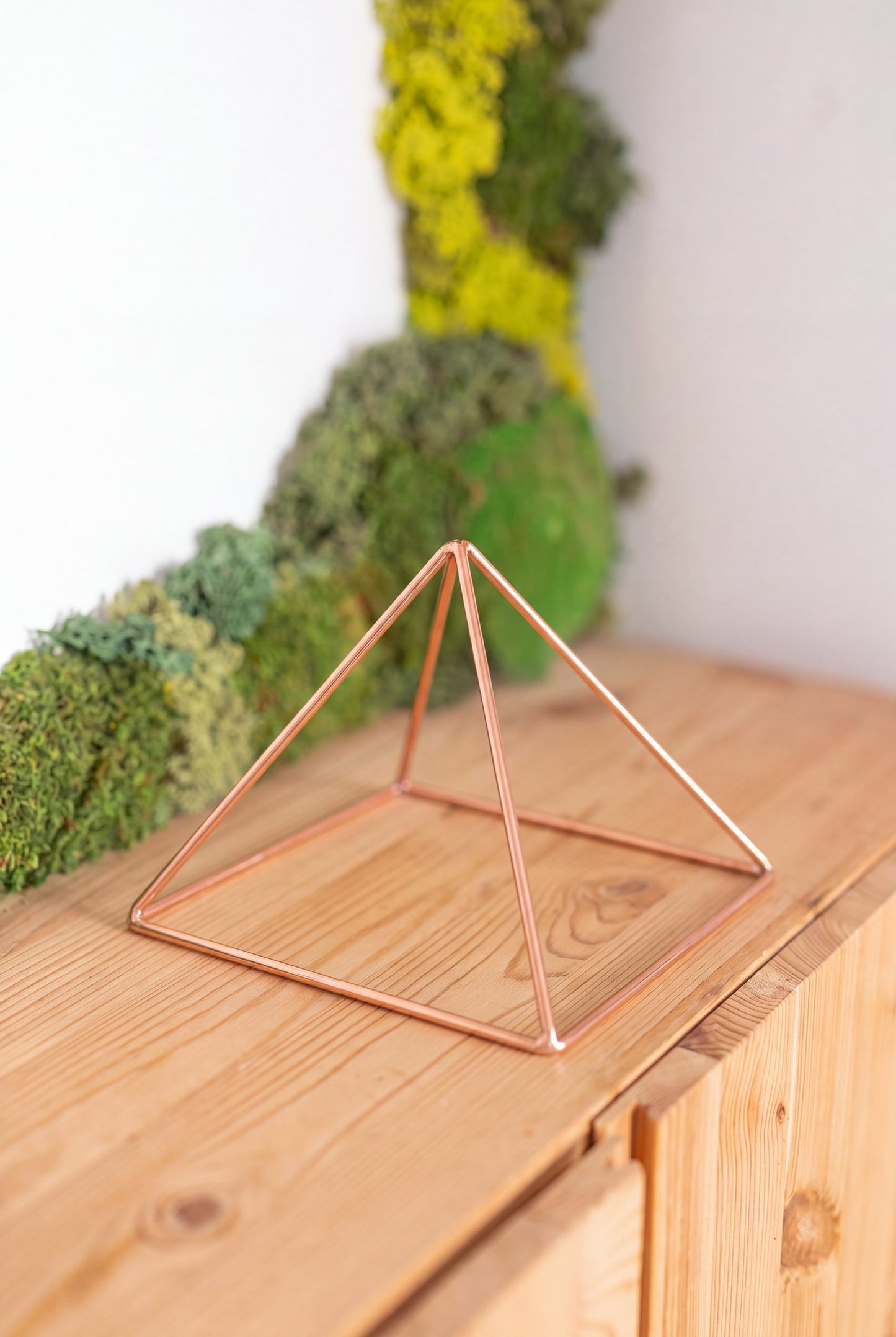 Pyramide énergisante en cuivre lisse Kopero Petite (14,56 cm) sur une armoire en pin devant un tableau de mousse