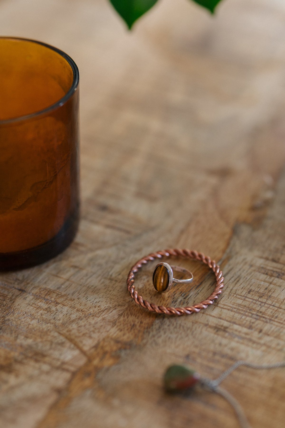 Kopero Koperen Tensorring, op een houten tafel met een ring met tijgeroog en een glazen kaarsenhouder