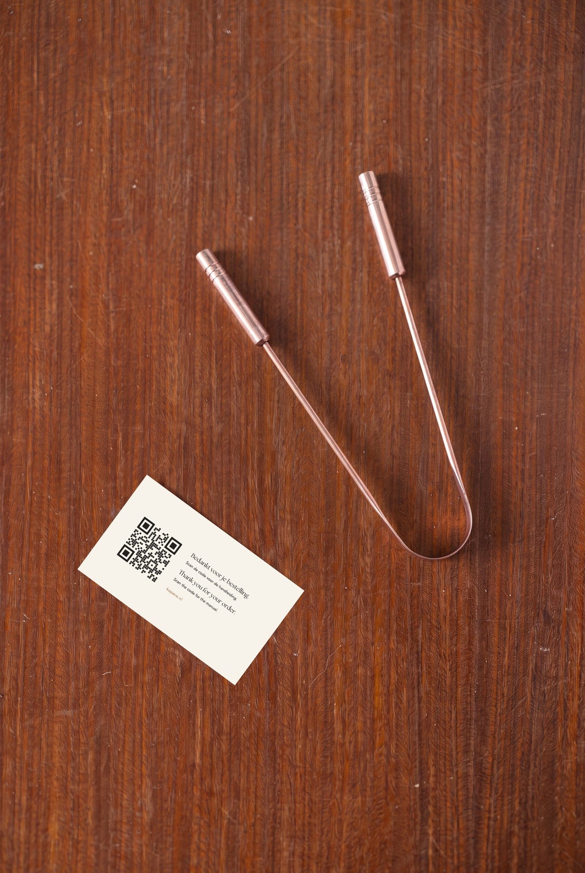 Racle-langue en cuivre Kopero vu de dessus sur du bois, avec carte de remerciement