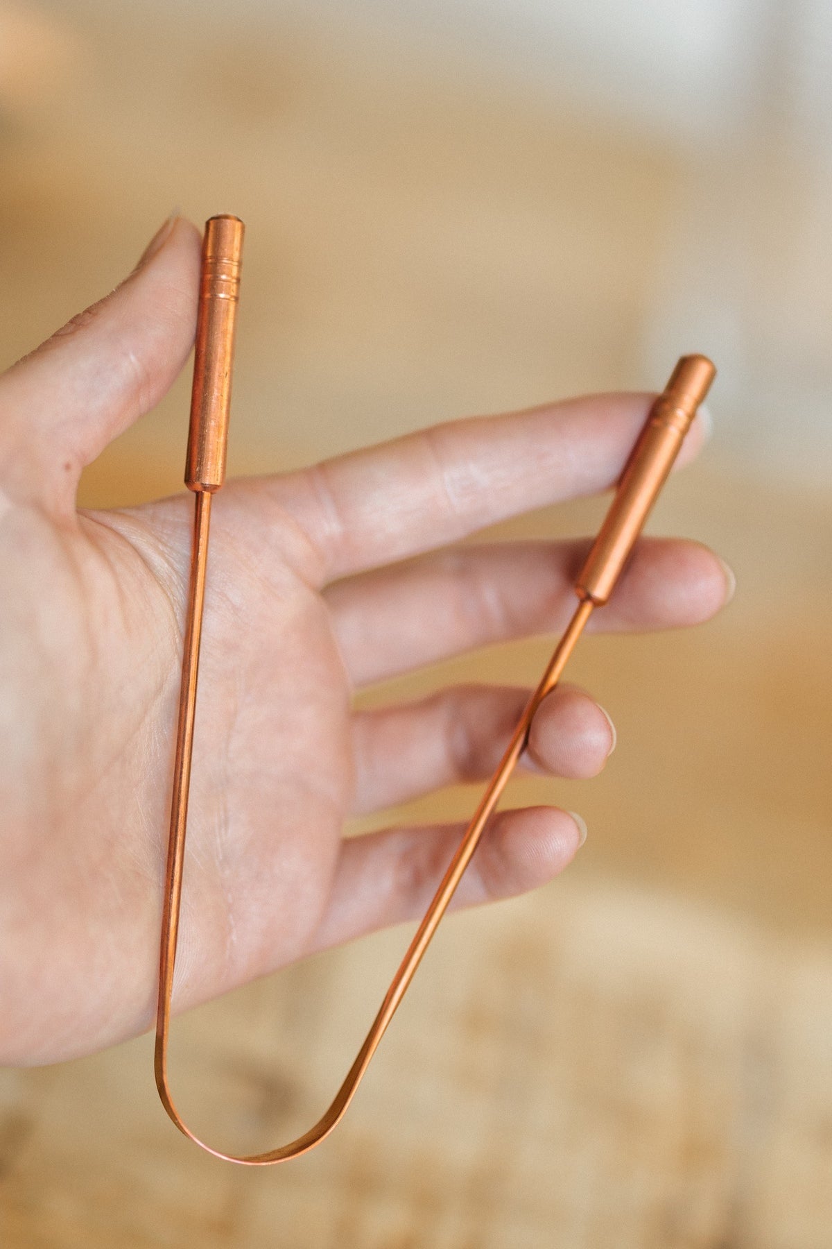 Kopero Koperen Tongschraper, in een open hand, met beide handvatten