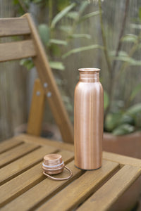 Bouteille d'eau en cuivre Kopero Lisse sur une chaise de jardin en bois, avec le bouchon à côté