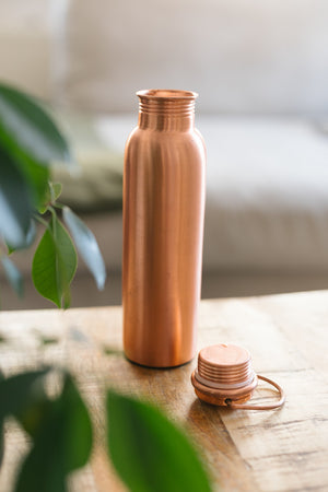 Kopero Koperen Waterfles Glad, staand op een houten tafel voor een bank, met de losse dop ernaast